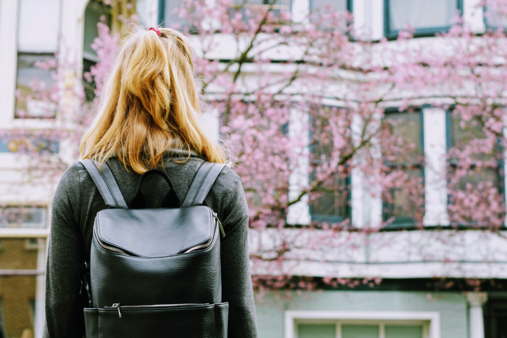 En student som står me ryggen till framför en vit byggnad och flera rosablommande körsbärsträd