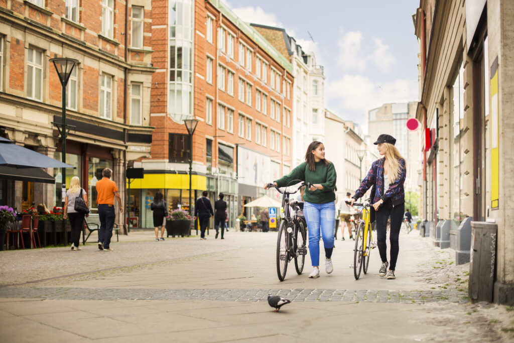 Two young women walking and pushing bicycles in old town
