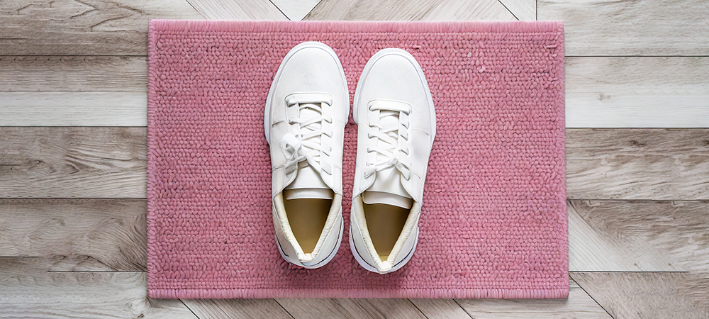 Ett par vita sneakers på en rosa dörrmatta fotograferad ovanifrån