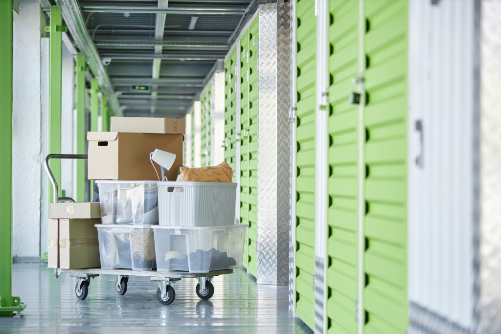 Background shot of dolly cart loaded with cardboard boxes storing personal belongings in hallway of self storage warehouse during moving out or apartment decluttering, copy space