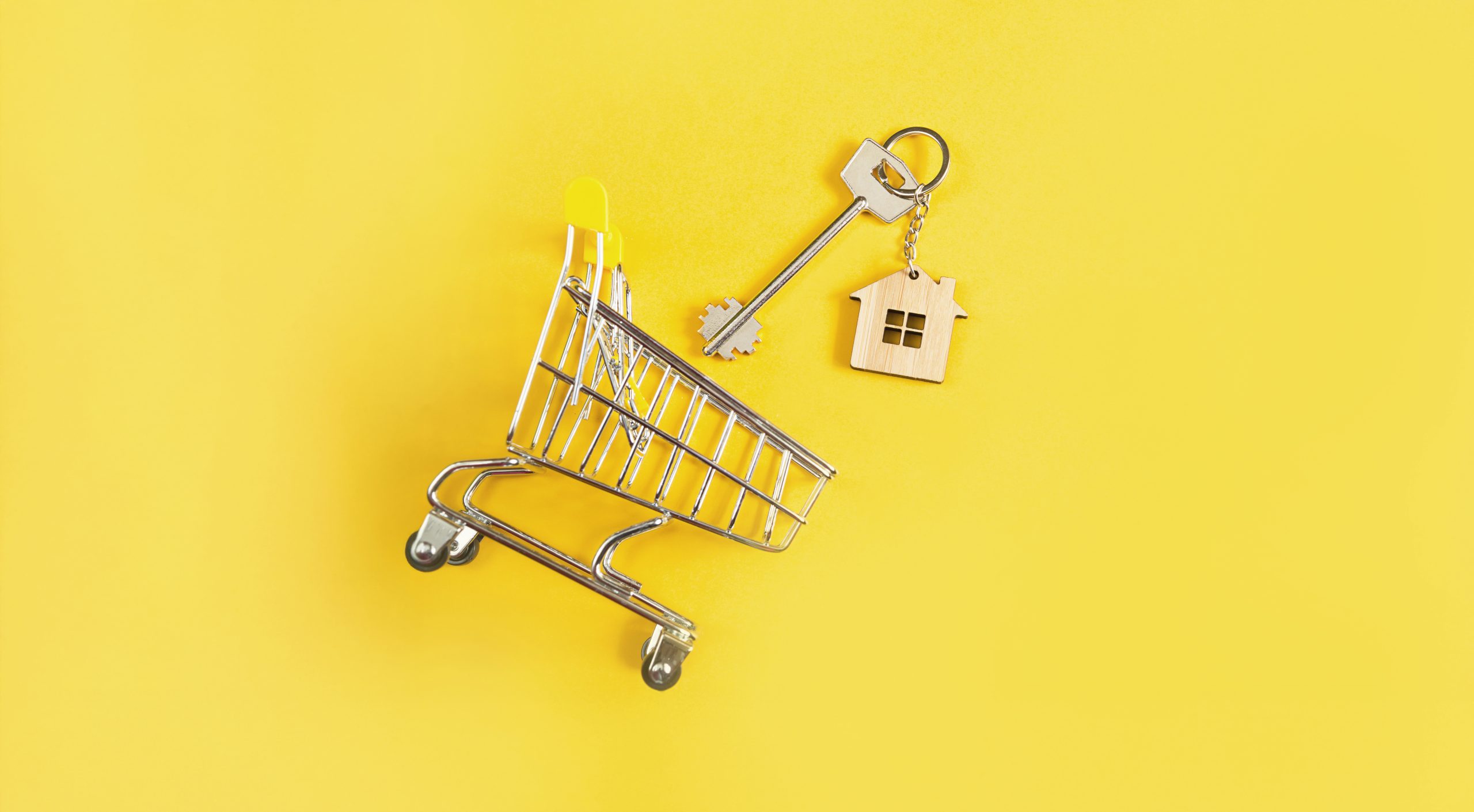 Key ring in the shape of wooden house with key on a yellow background and shopping cart. Mortgage, rent and purchase real estate, spring and summer offer for construction. Copy space