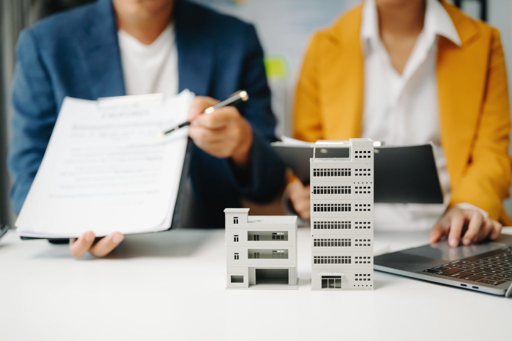 Real estate broker agent presenting and consult to customer to decision making sign insurance form agreement, home model, concerning mortgage loan offer in office
